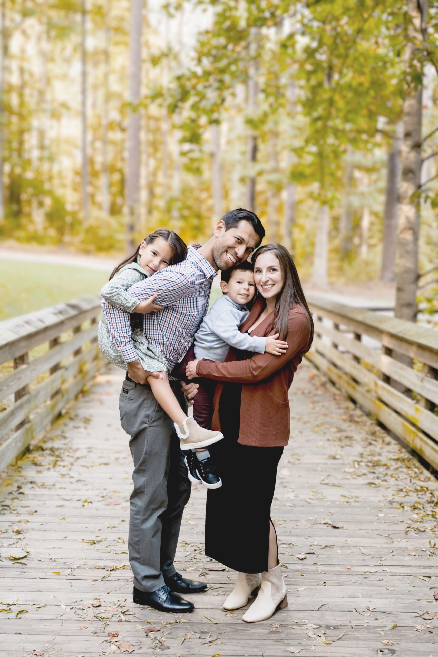 A happy family of four stand in a wooden boardwalk laughing while the toddlers climb on mom and dad. before visiting a kid's life