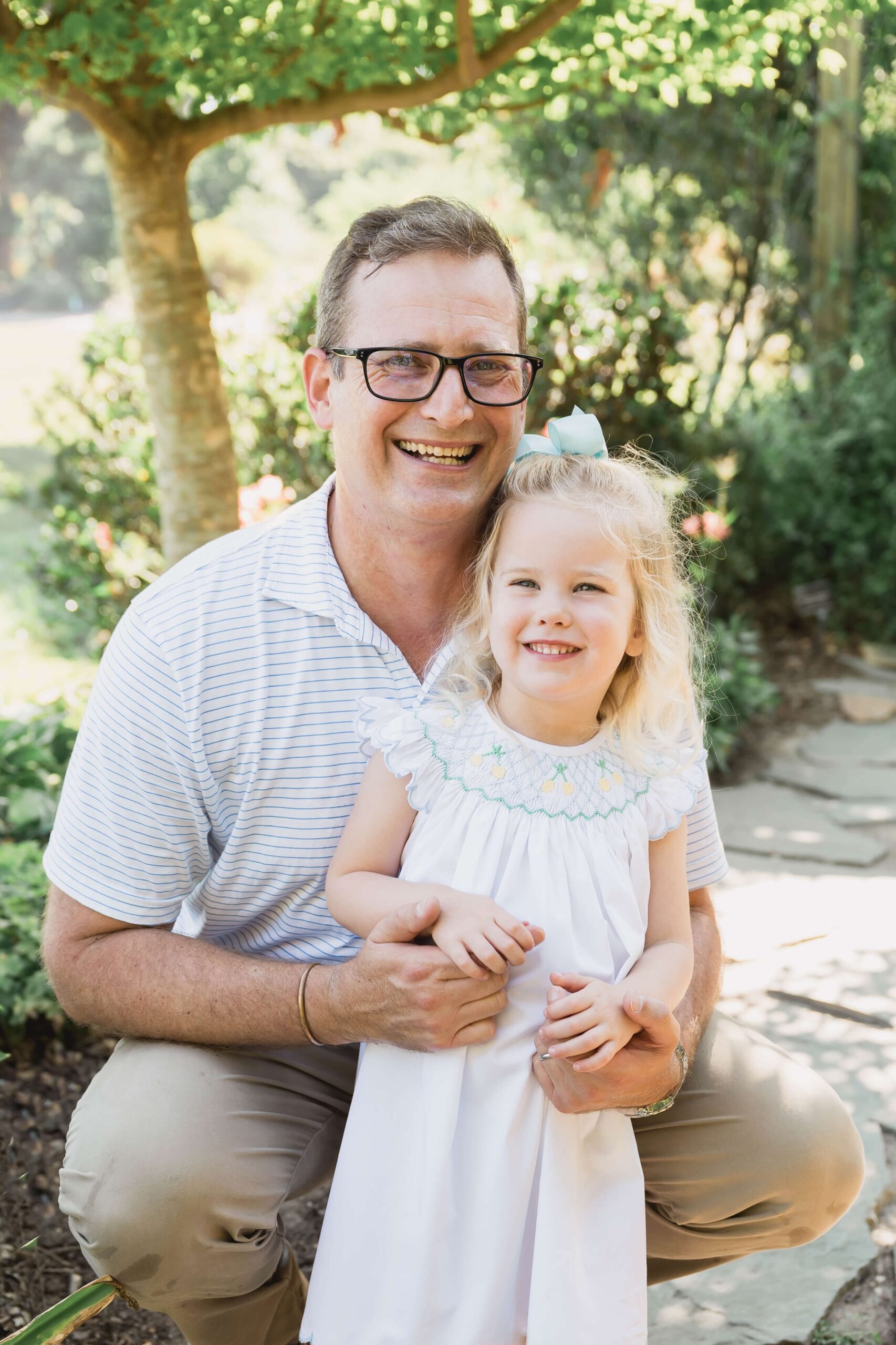 A happy father hugs his toddler daughter while laughing in a garden path while visiting apex nc parks