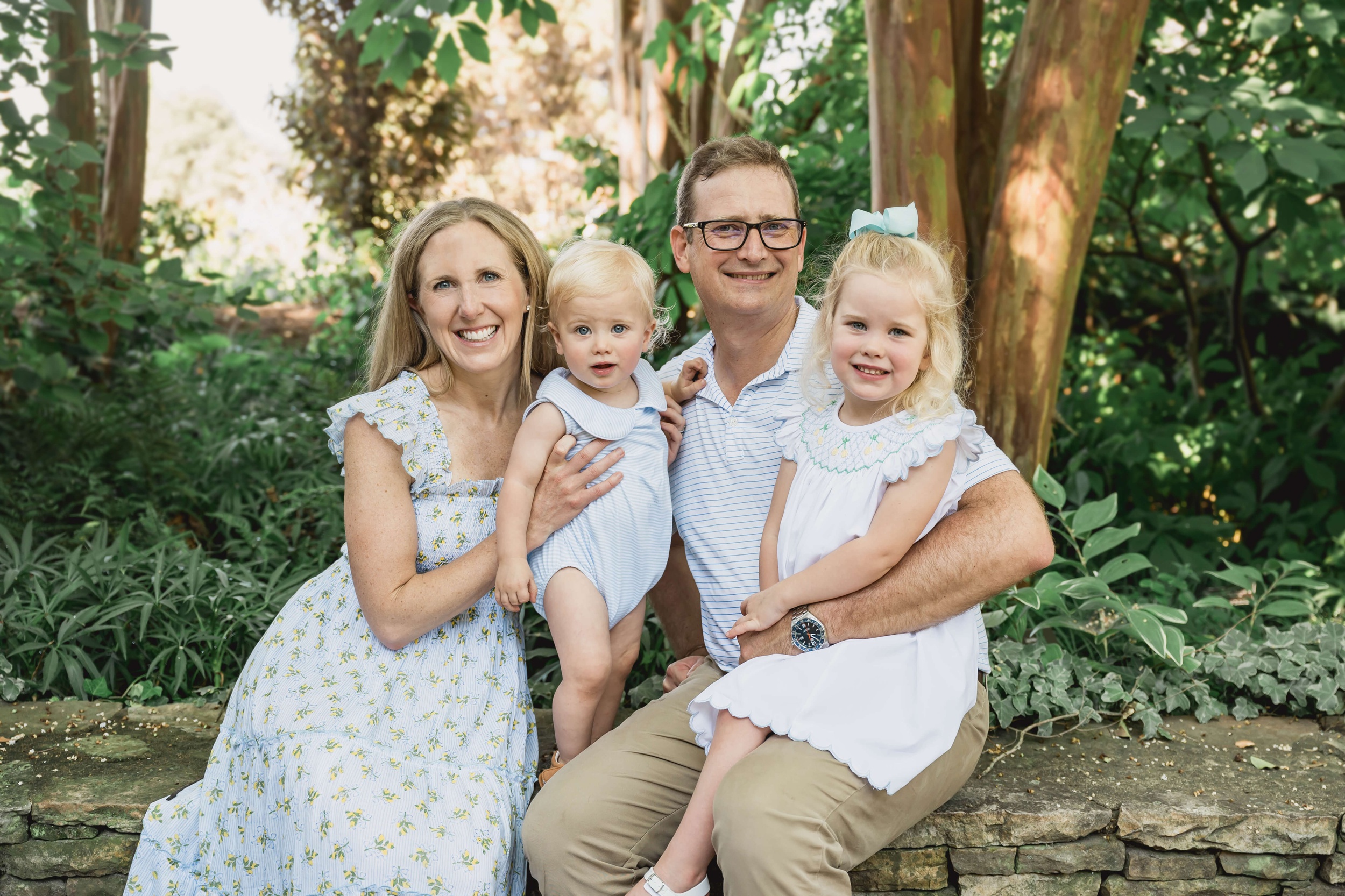 A happy family of four sit on a stone garden wall smiling before visiting apex summer camps