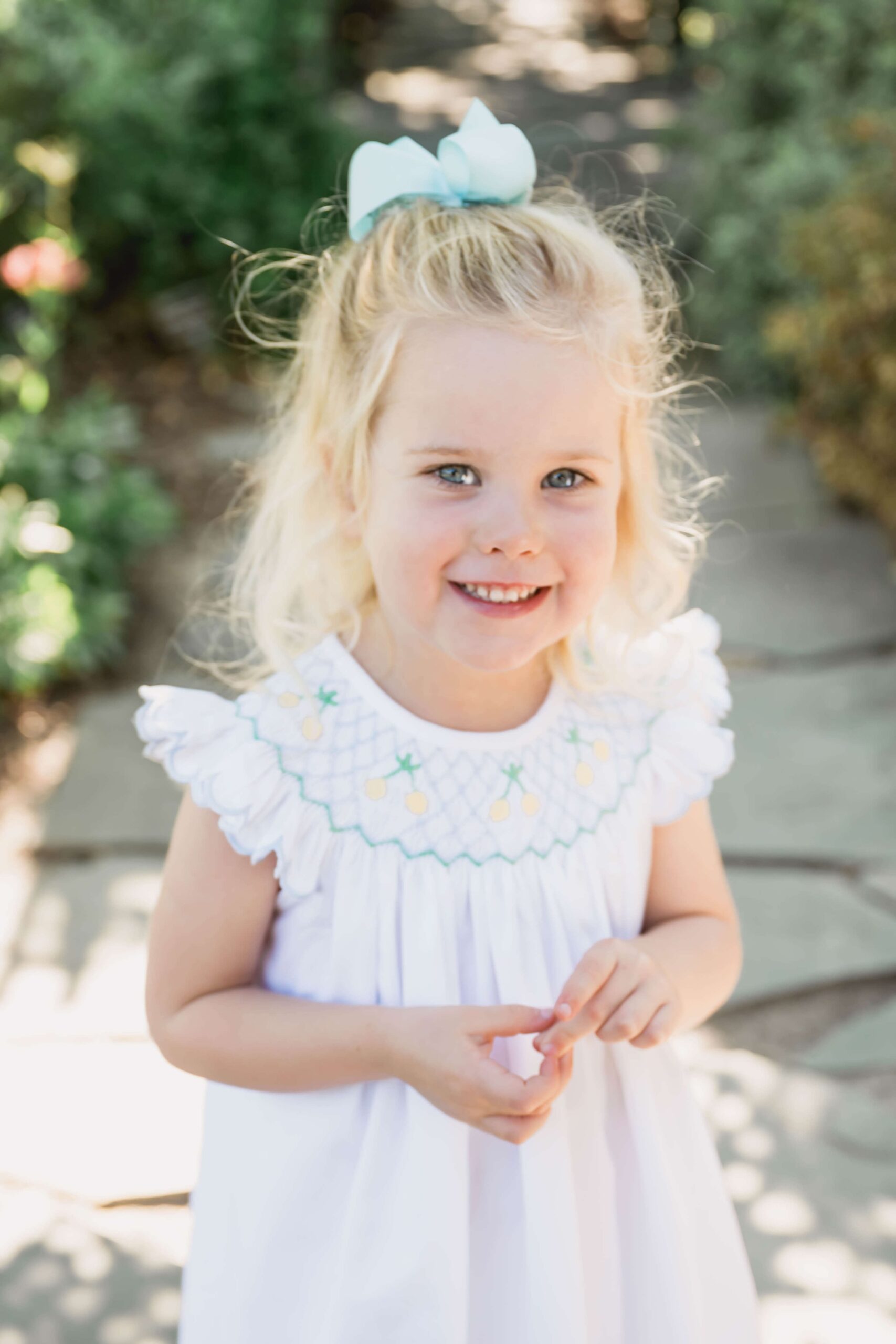 A toddler girl in a white dress smiles while exploring a garden before finding apex summer camps