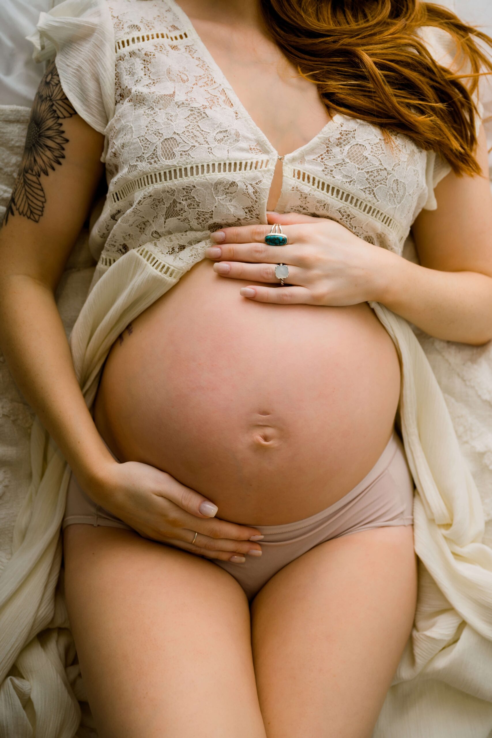 Details of a mother to be holding her bump while laying on a bed after visiting birthing centers in raleigh nc