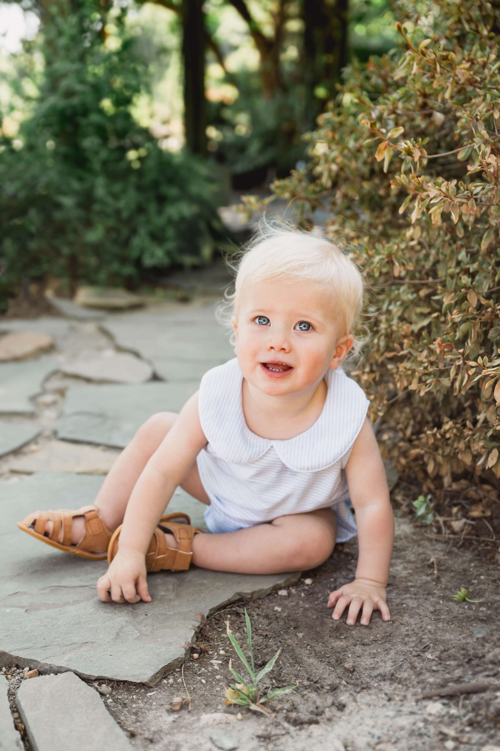 A happy toddler plays in some dirt while sitting on a garden path after visiting chapel hill pediatricians