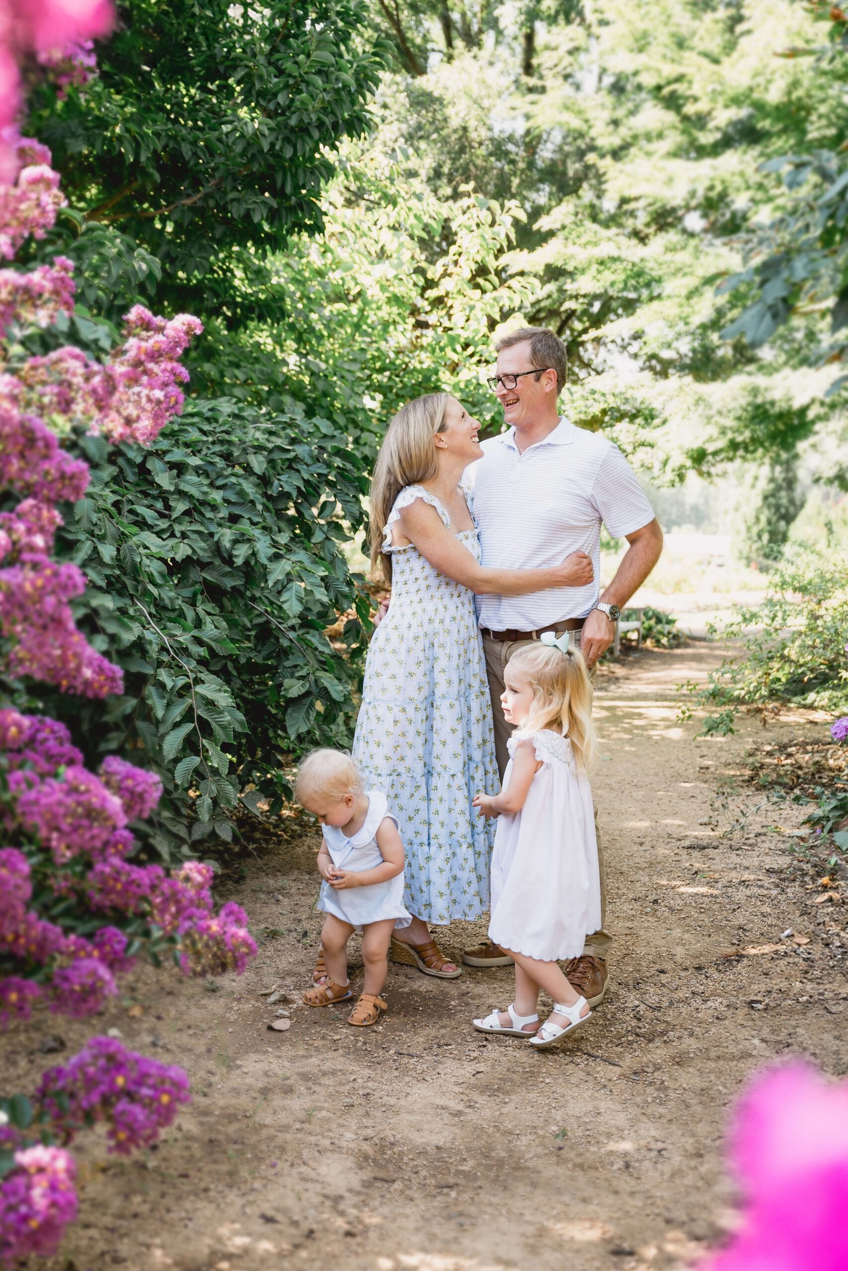 Happy mom and dad hug while their toddler son and daughter play in a garden trail after visiting chapel hill pediatricians