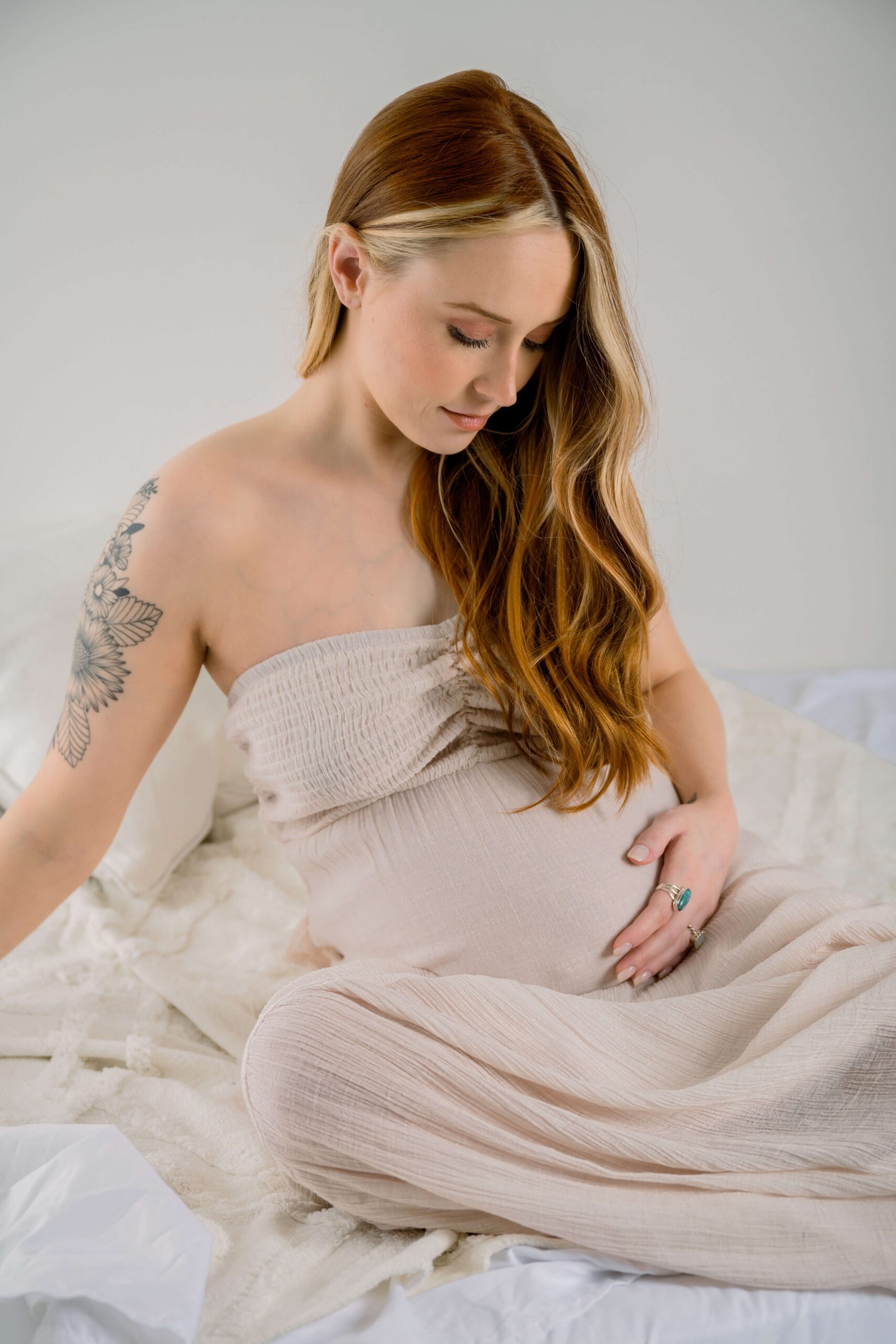 A pregnant woman glances down at her bump with her hand on in while sitting on a bed after visiting city of oaks midwifery