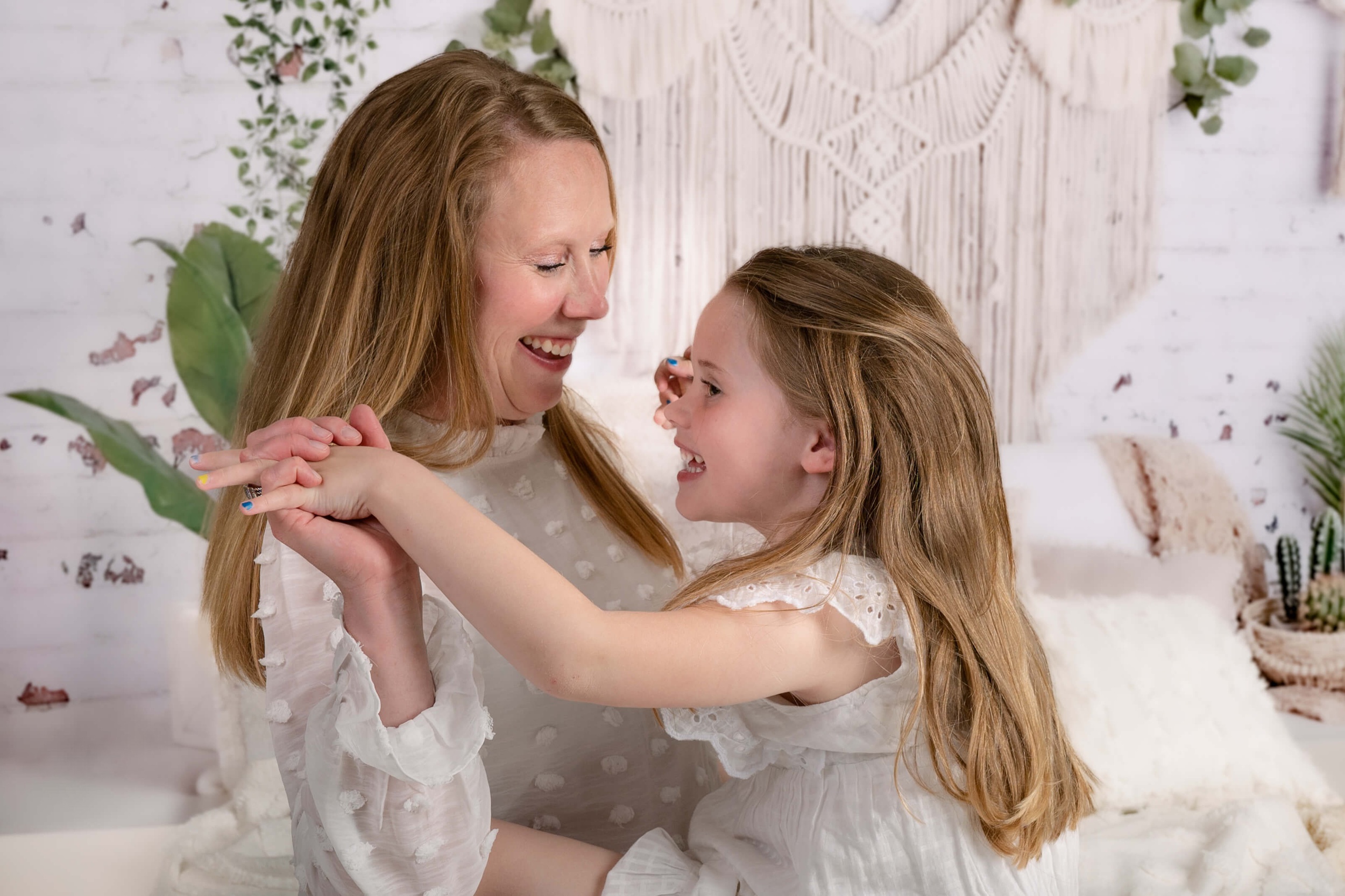 A happy toddler girl holds hands and plays with mom while sitting on a bed and laughing