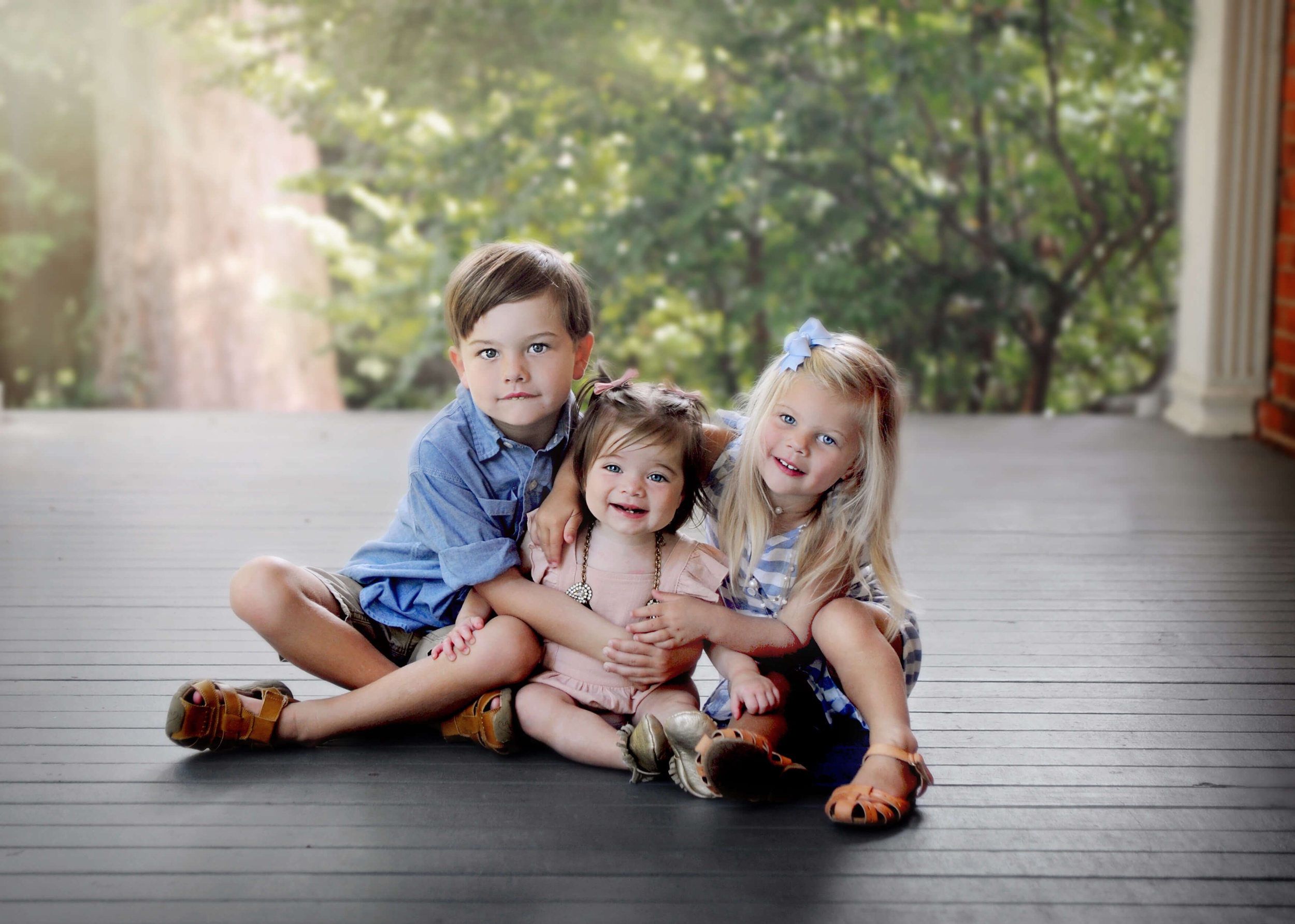 Happy toddler brother and sister hug onto their younger sister while sitting on a porch at sunset before visiting parks in raleigh nc