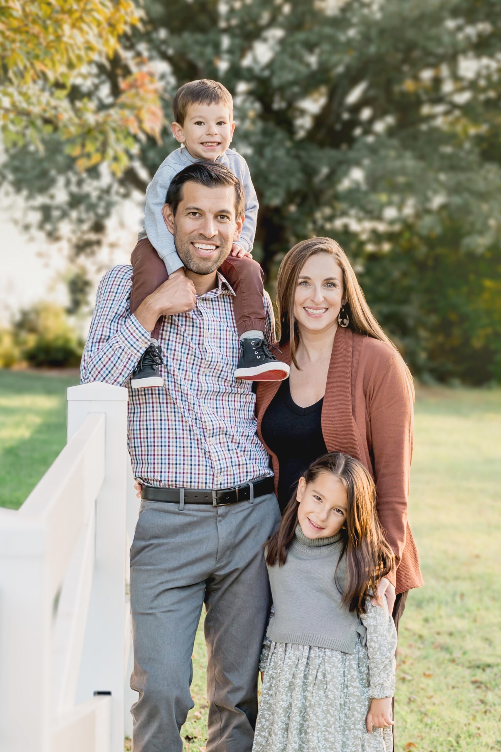 A happy family of 4 stand by a white fence in a park at sunset while visiting parks in raleigh nc