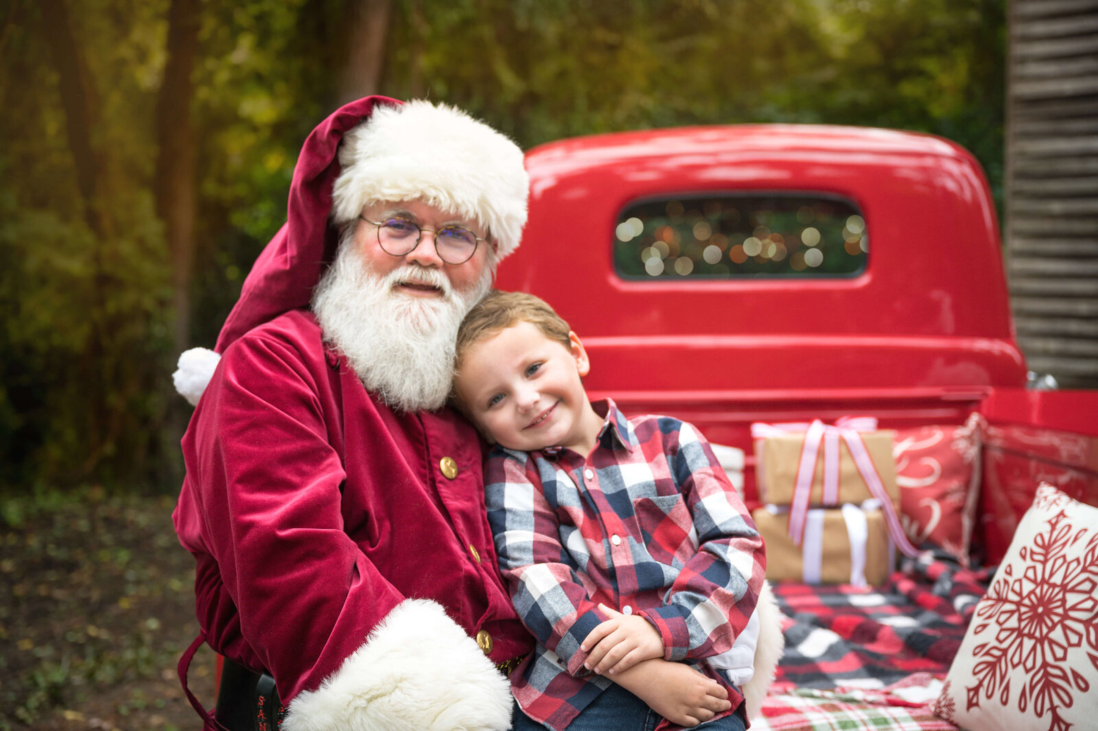 A happy young boy leans into santa while sitting in a red vintage truck while visiting a raleigh christmas tree farm