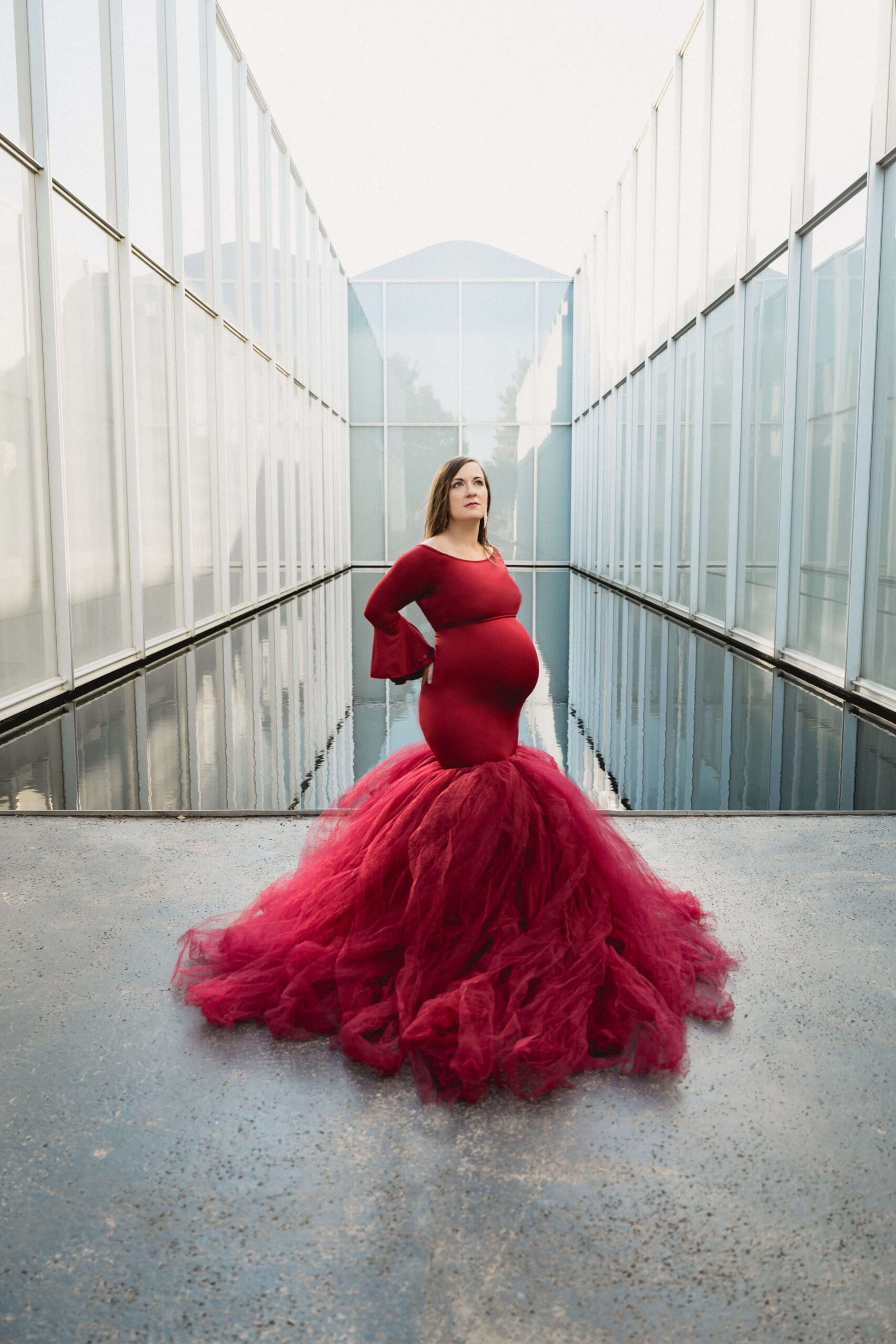 A mother to be in a flowing maternity gown stands in a modern building with a pond after meeting raleigh doulas