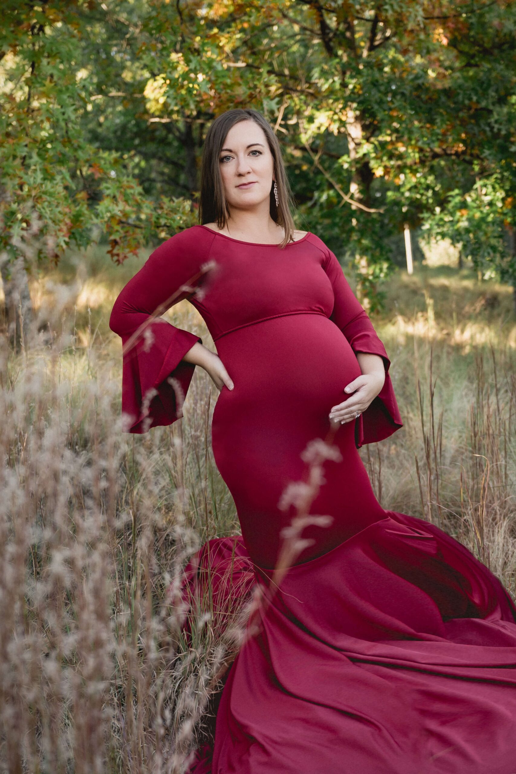 A mother to be in a red maternity gown stands in some tall golden grass holding her bump after meeting raleigh doulas