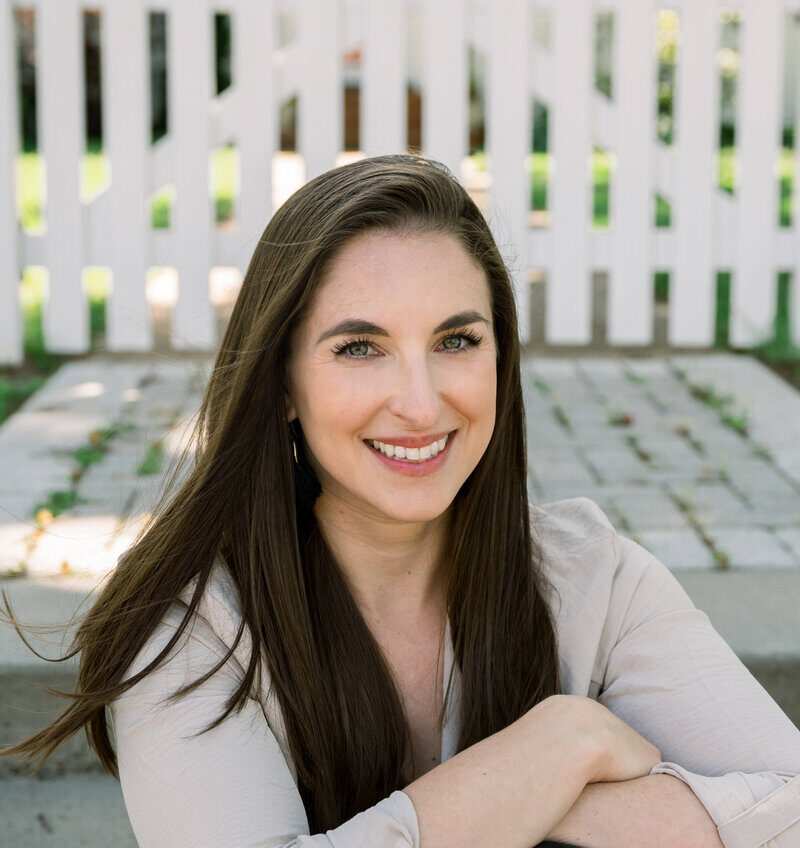 A woman in a tan jacket sits on garden steps for a raleigh headshot photographer