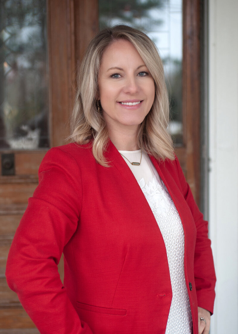 An image from a raleigh headshot photographer of a woman in a red jacket and white blouse standing with hands on her hips on a porch