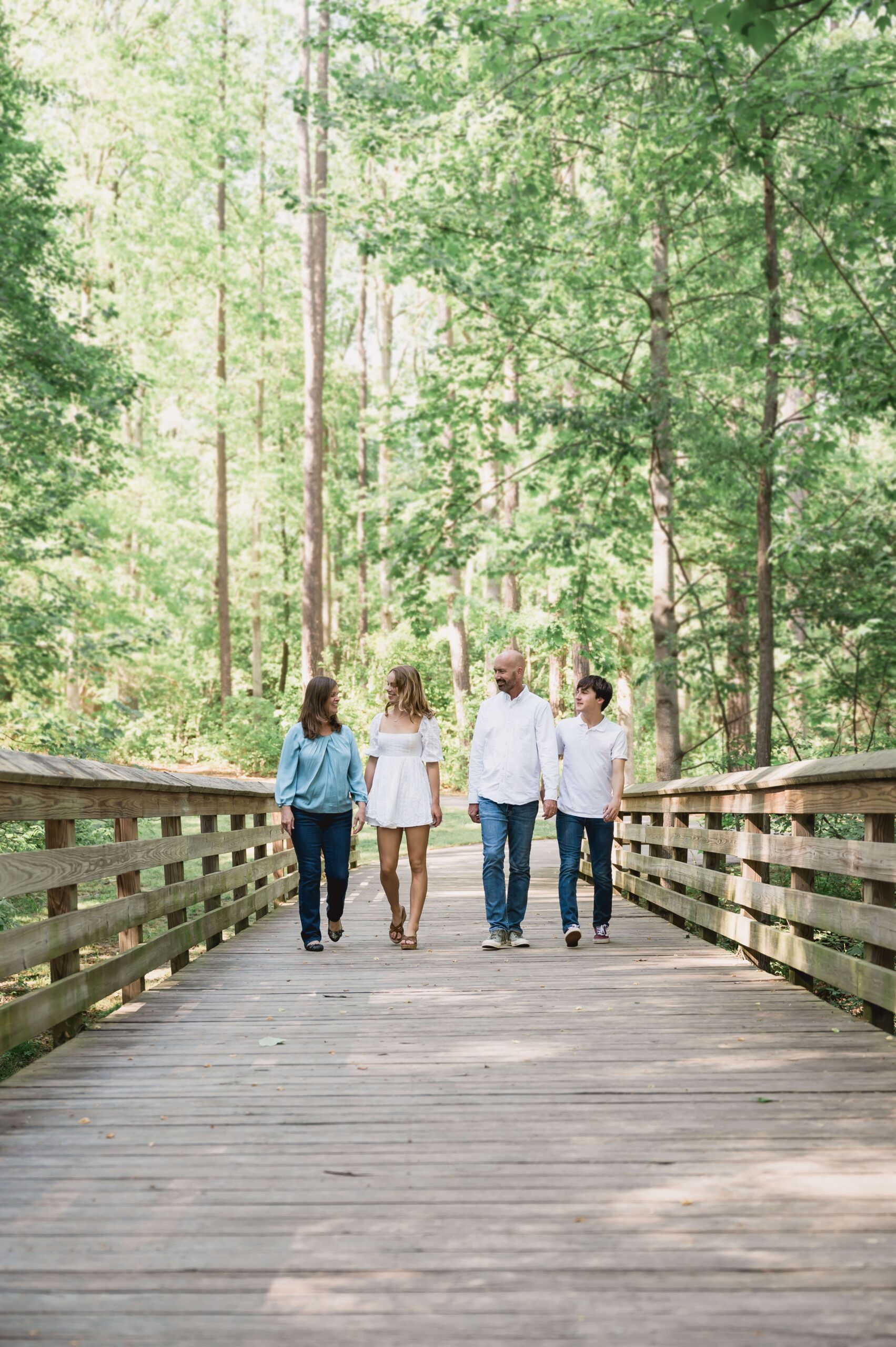 A happy family of 4 walk on a wide boardwalk in a forest before attending raleigh nc track out camps