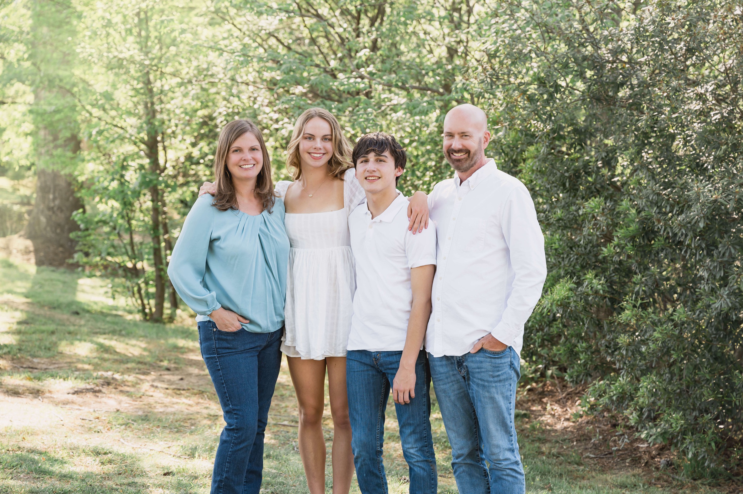 Proud parents of teen son and daughter stand in a park with arms around each other in white and blue before some raleigh nc track out camps