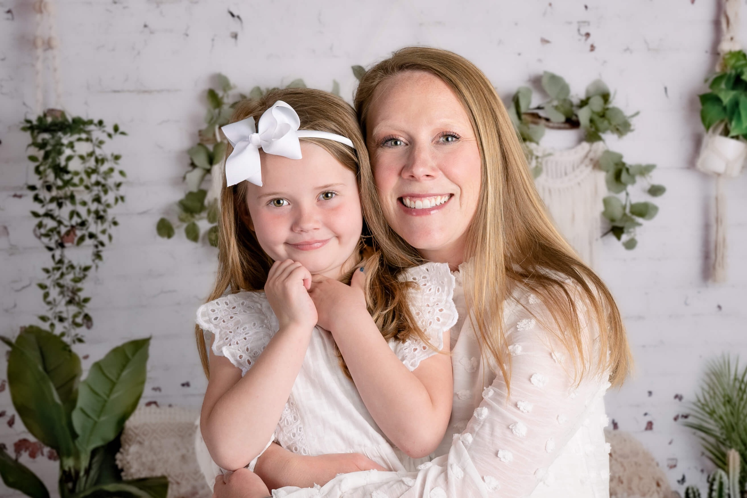 A happy toddler girl sits in mom's lap smiling in a white dress before attending raleigh summer camps