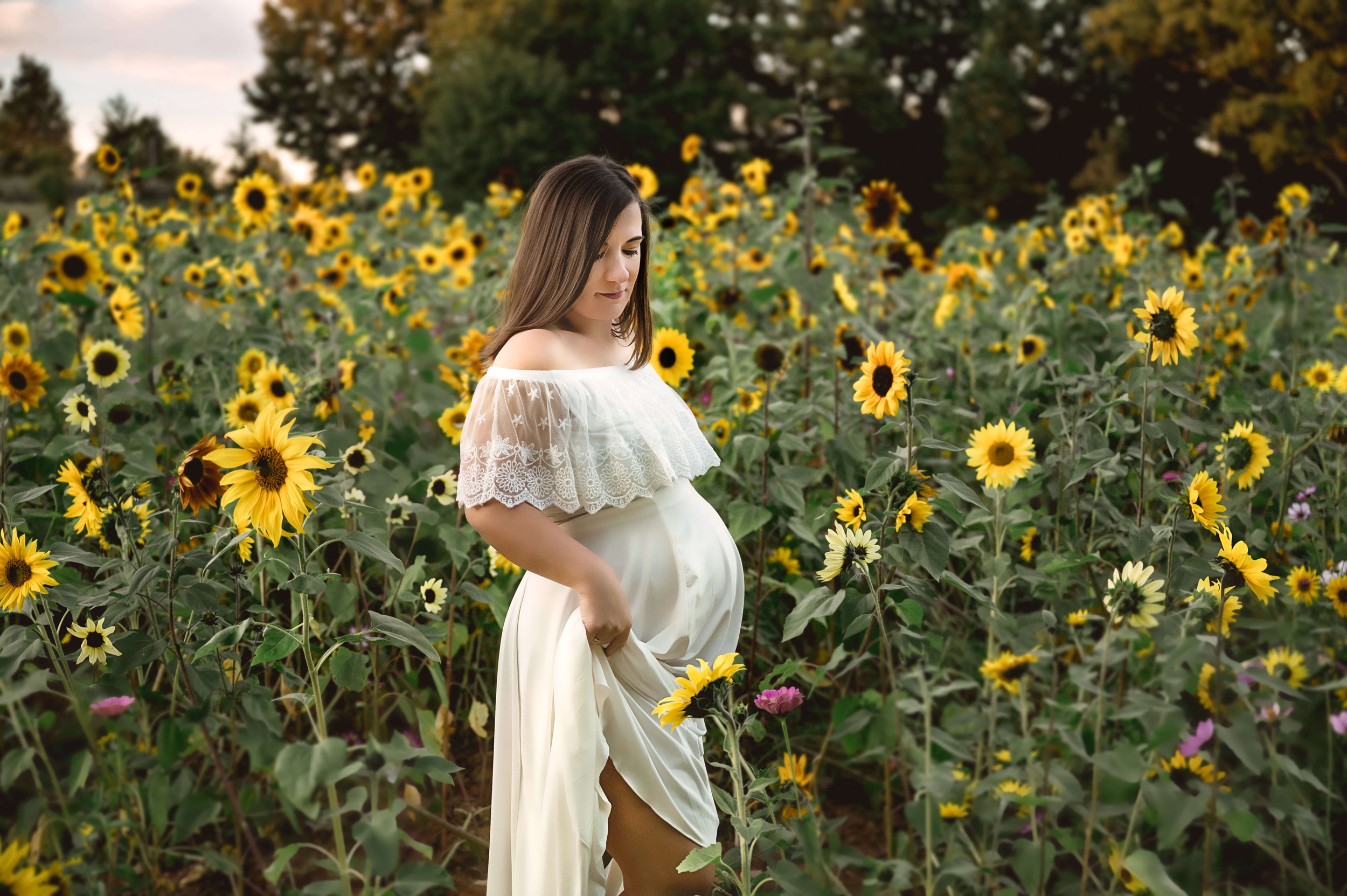 A mom to be in a white maternity gown explores a field of sunflowers after visiting unc rex women's center