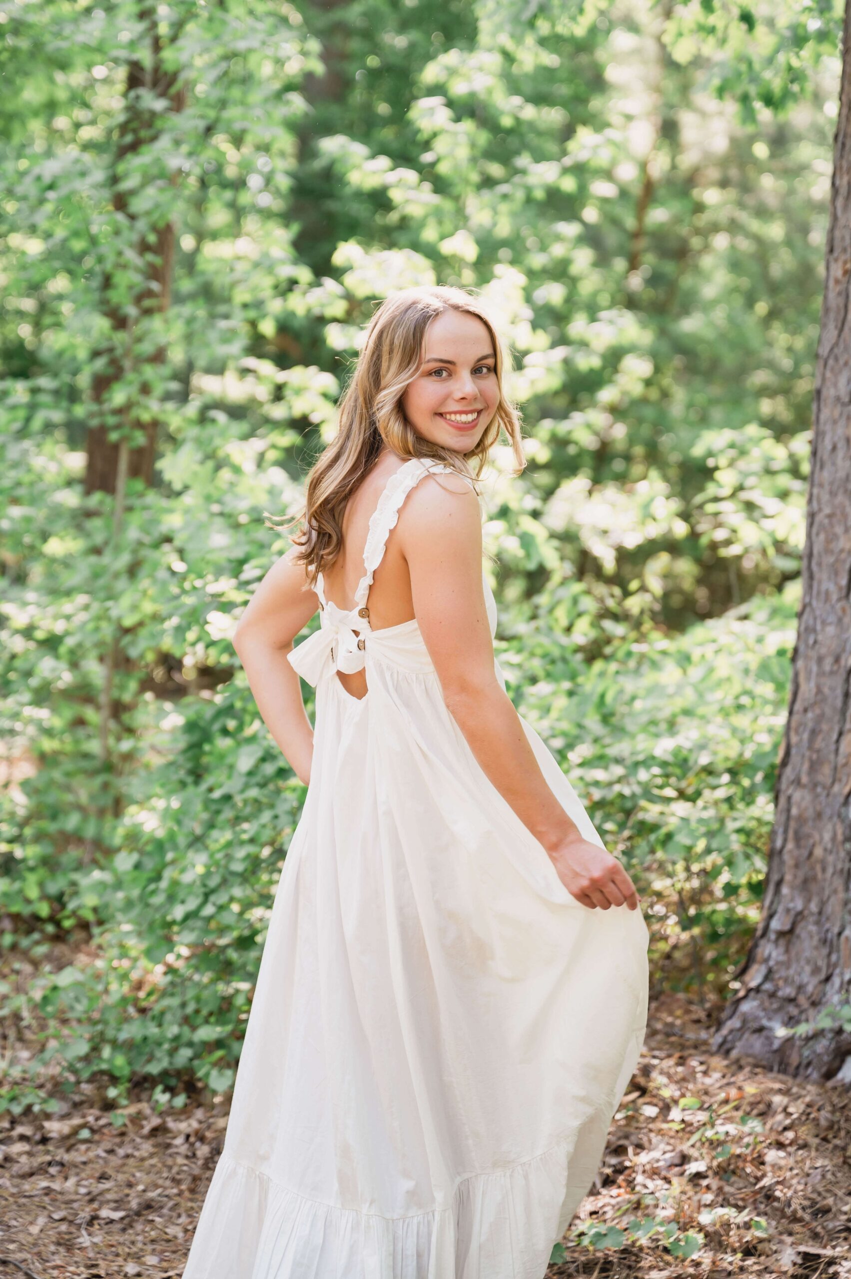 A wake county private schools senior in a long white dress hikes in a forest while smiling