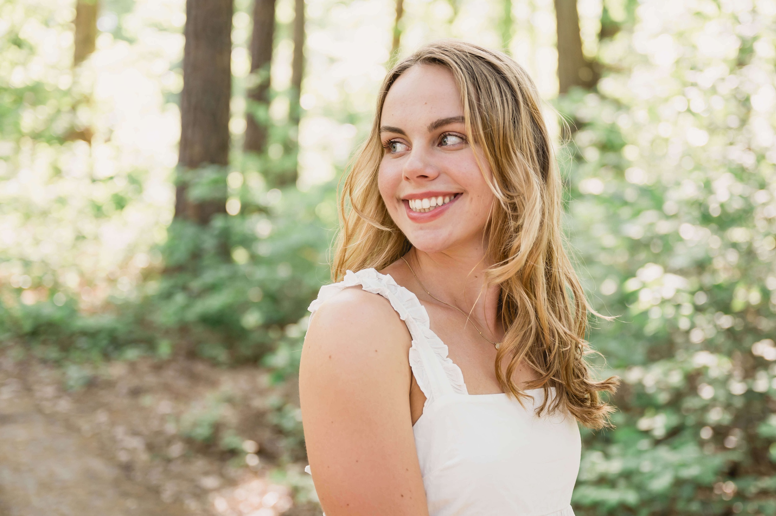 A wake county private schools senior smiles over her shoulder while hiking in a white dress